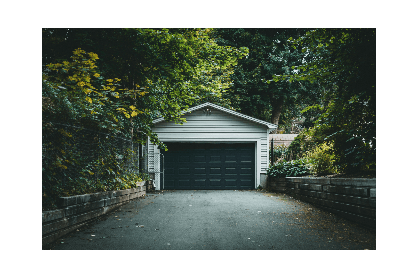 A dark blue house with a white garage door and a long concrete driveway against a clear blue sky.
