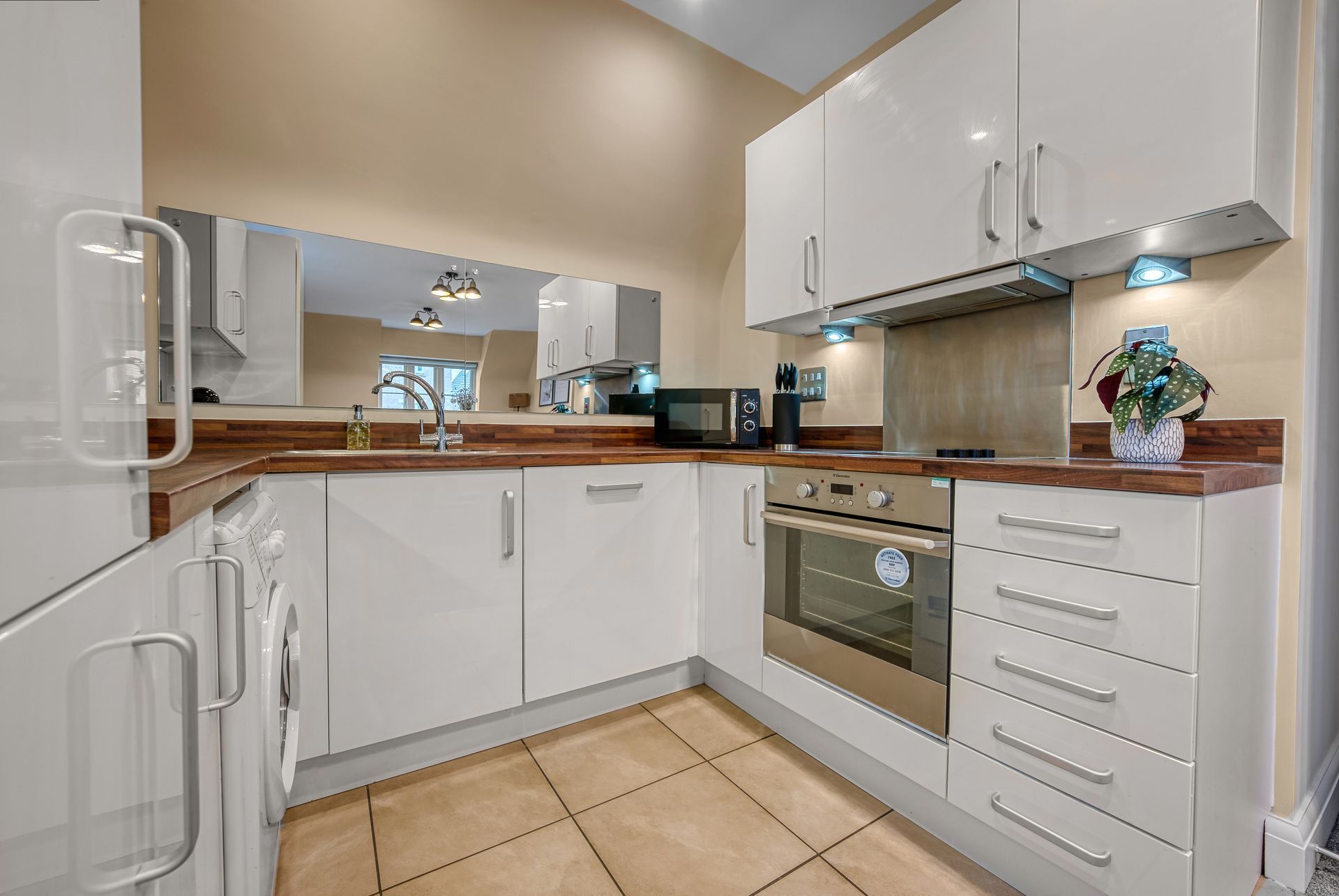 White modern kitchen with glossy cabinets, appliances, and brown countertops.
