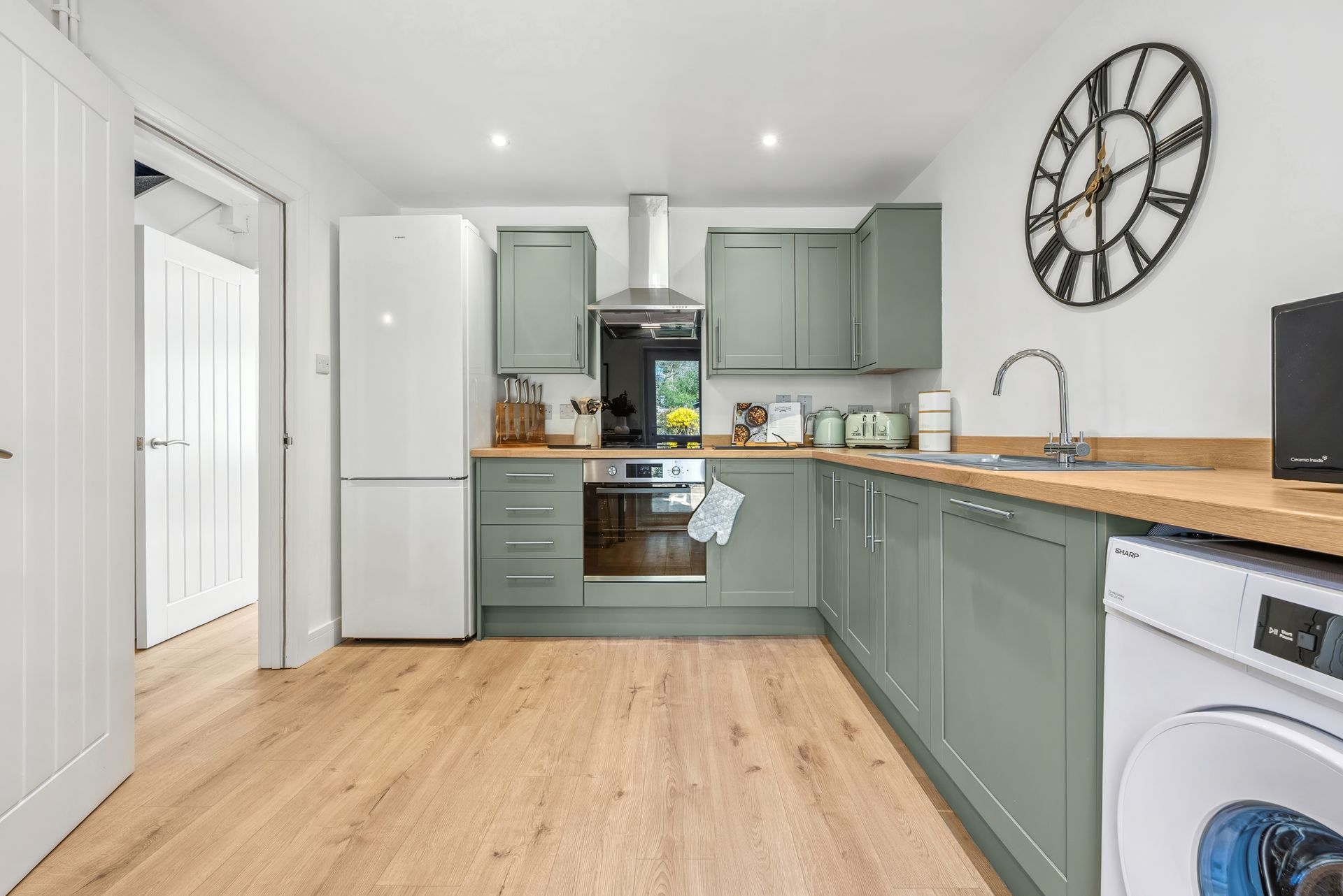 Green kitchen with wooden countertops, white appliances, and a large clock.