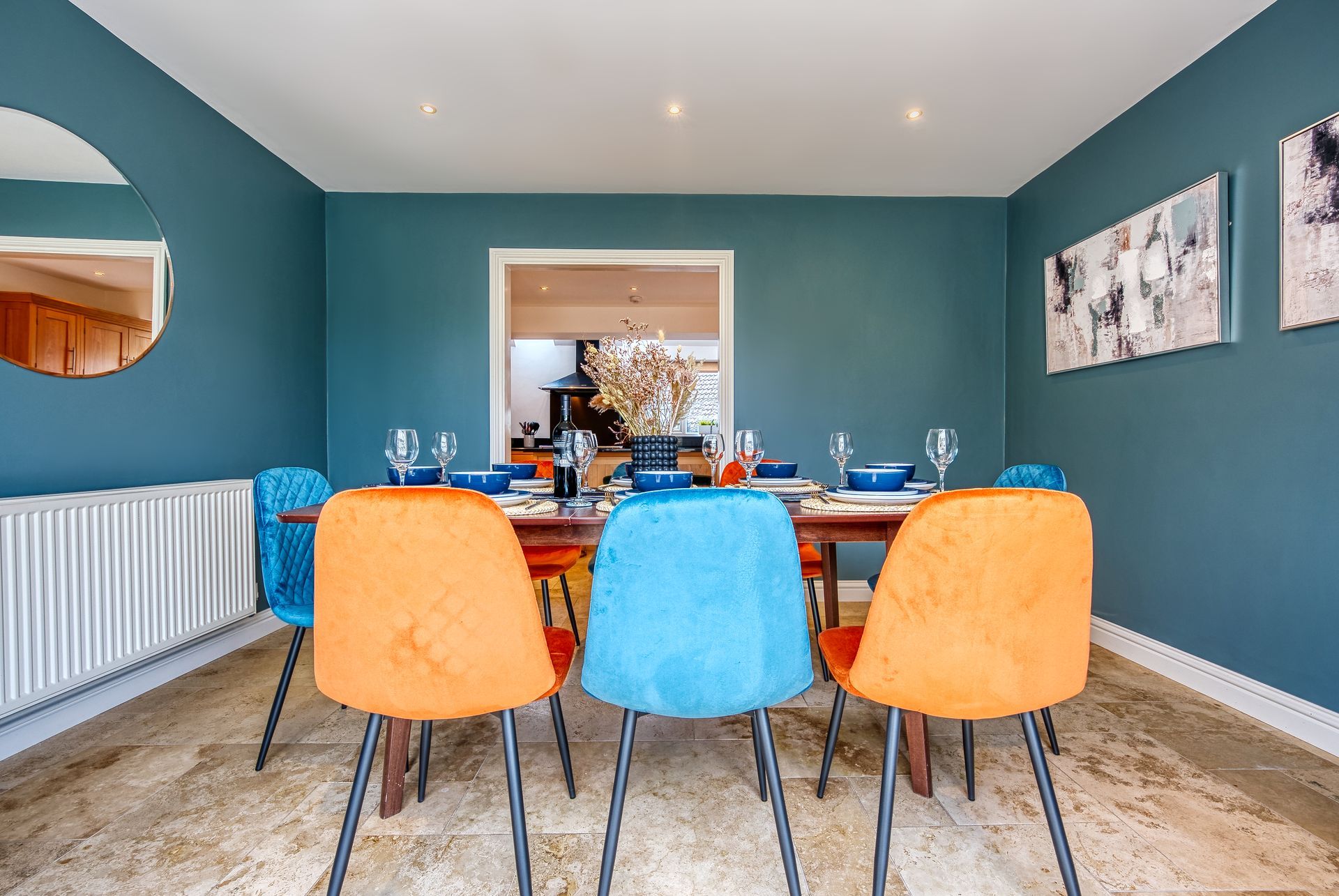 Dining room with teal walls, a wooden table, colorful chairs, and artwork.