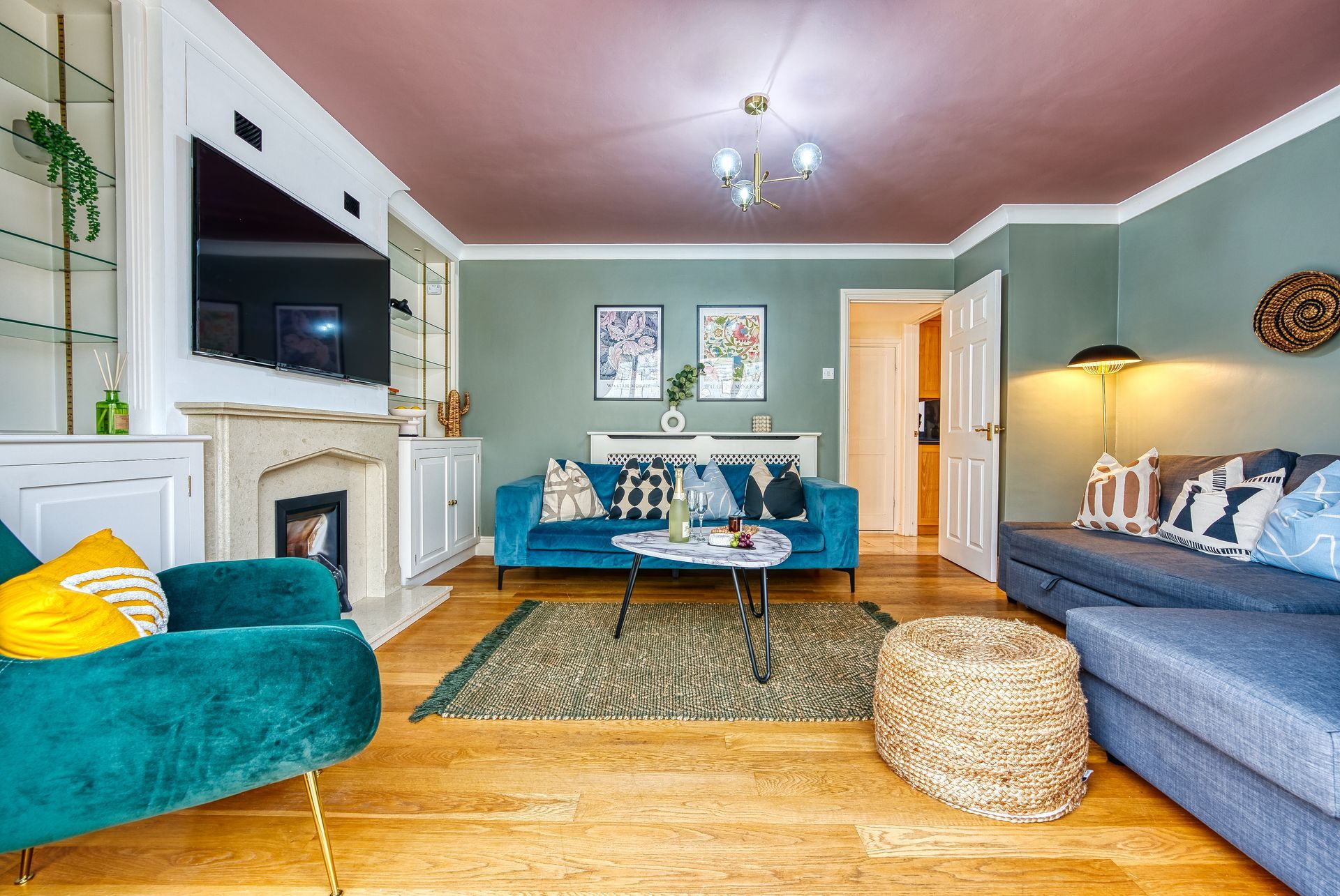 Living room with teal walls, pink ceiling, blue sofa, and wooden floor.