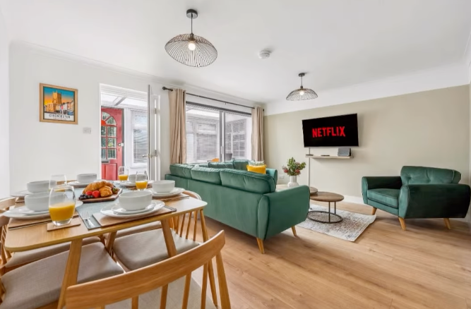 Living room with dining area. Teal couch, armchair, wooden table set for meal, TV, and open doorway.