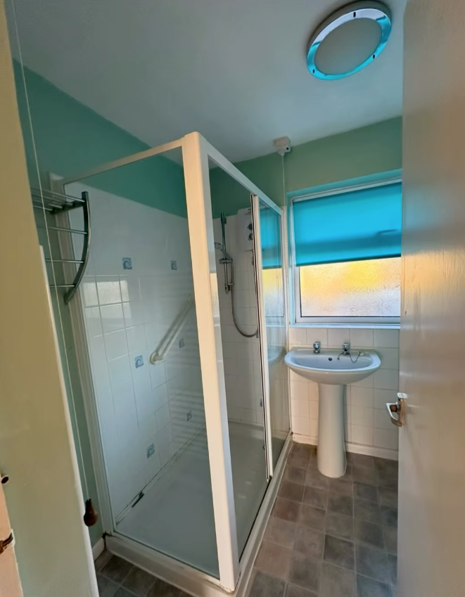 Bathroom with glass shower, sink, and window. Turquoise wall paint and blue blind.