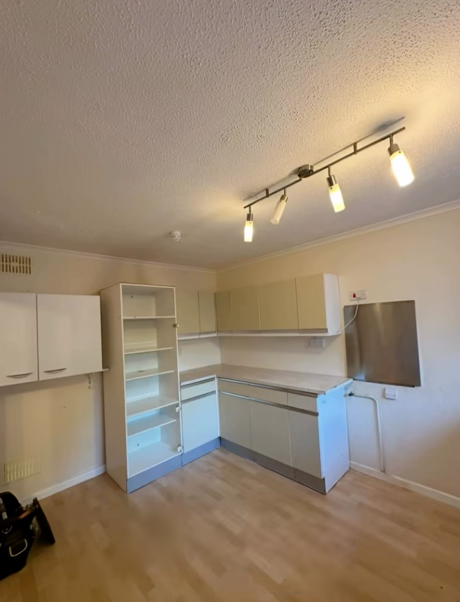 Empty kitchen with white cabinets, light wood floor, and track lighting.