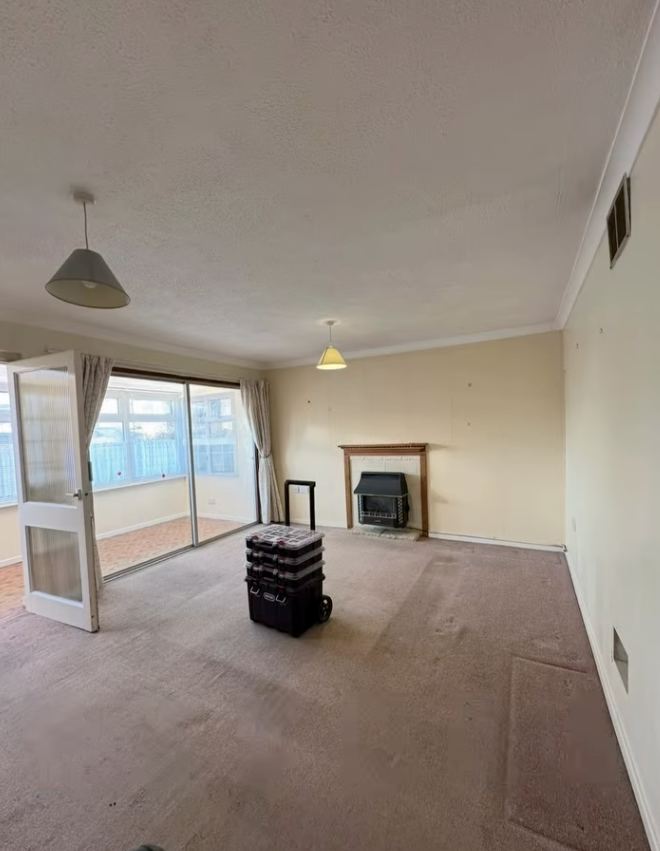 Empty living room with worn beige carpet, sliding glass doors, fireplace, and two overhead lights.
