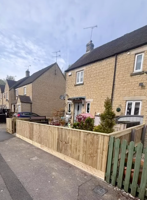 Row of beige stone houses with a wooden fence in front, gray sky overhead.