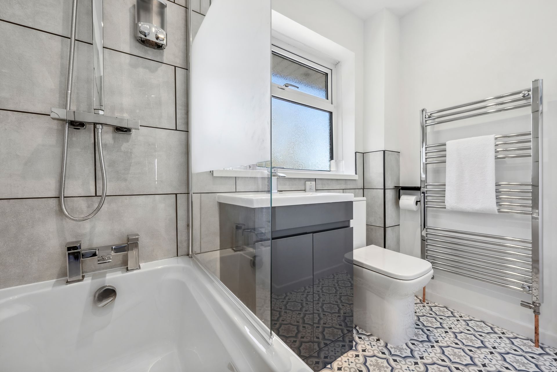 Bathroom with gray and white tile, shower, sink, toilet, and towel rack.