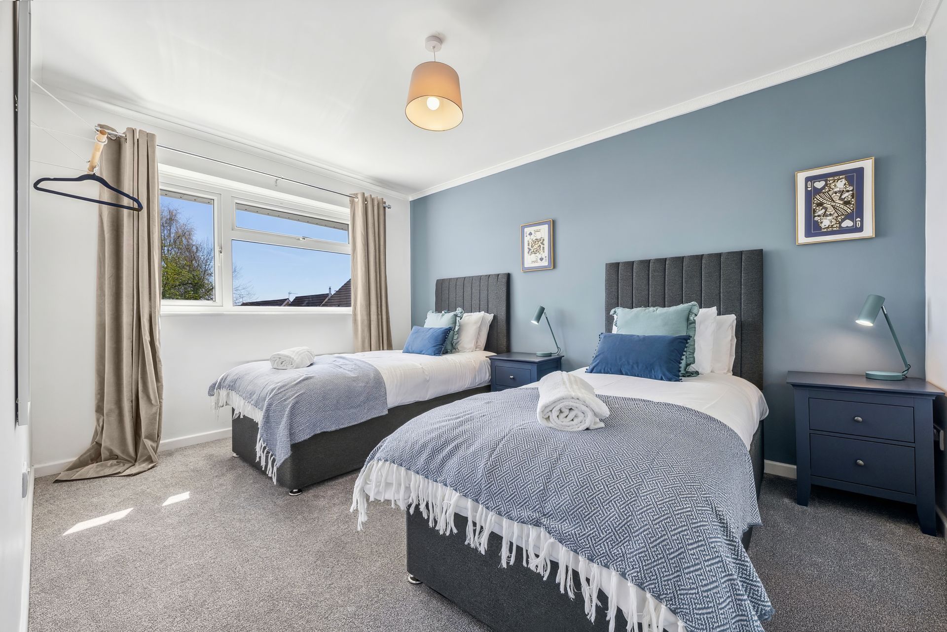 Bedroom with two twin beds, blue walls, window, lamps, and nightstand.