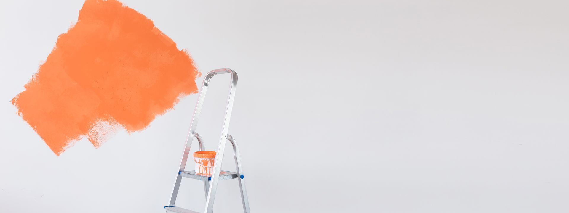 A white wall with a partial orange paint swatch and a metal ladder with a paint can.