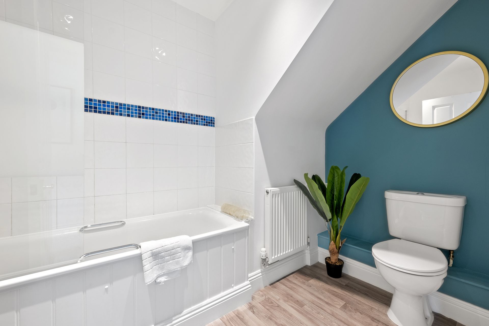 Bathroom with white tub, blue accent wall, toilet, and a round mirror.