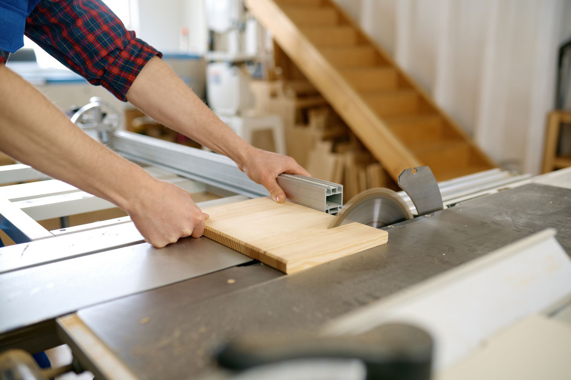 Person using a table saw to cut a wooden board in a workshop.
