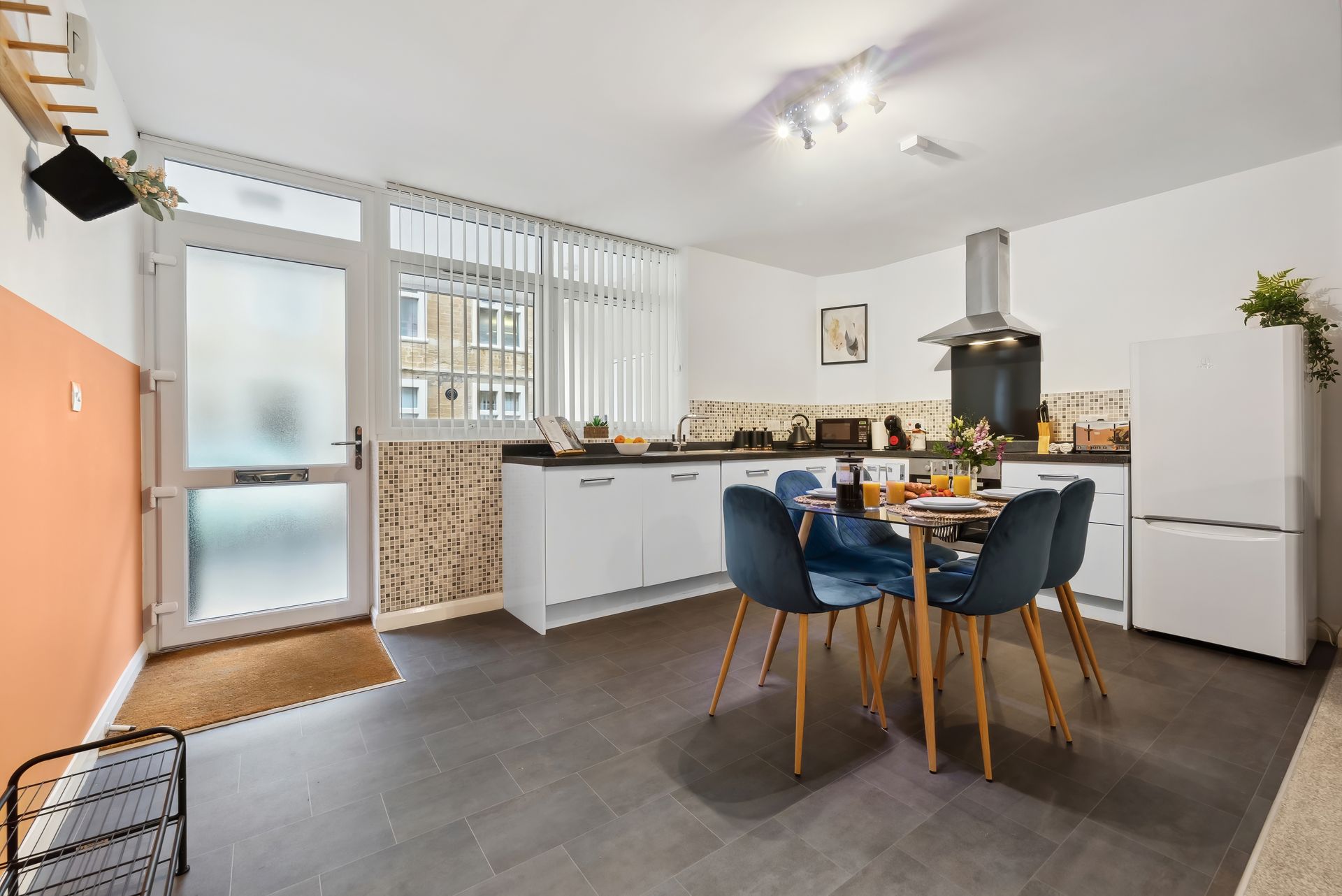 Kitchen with white cabinets, blue chairs around a table, and a door leading outside.