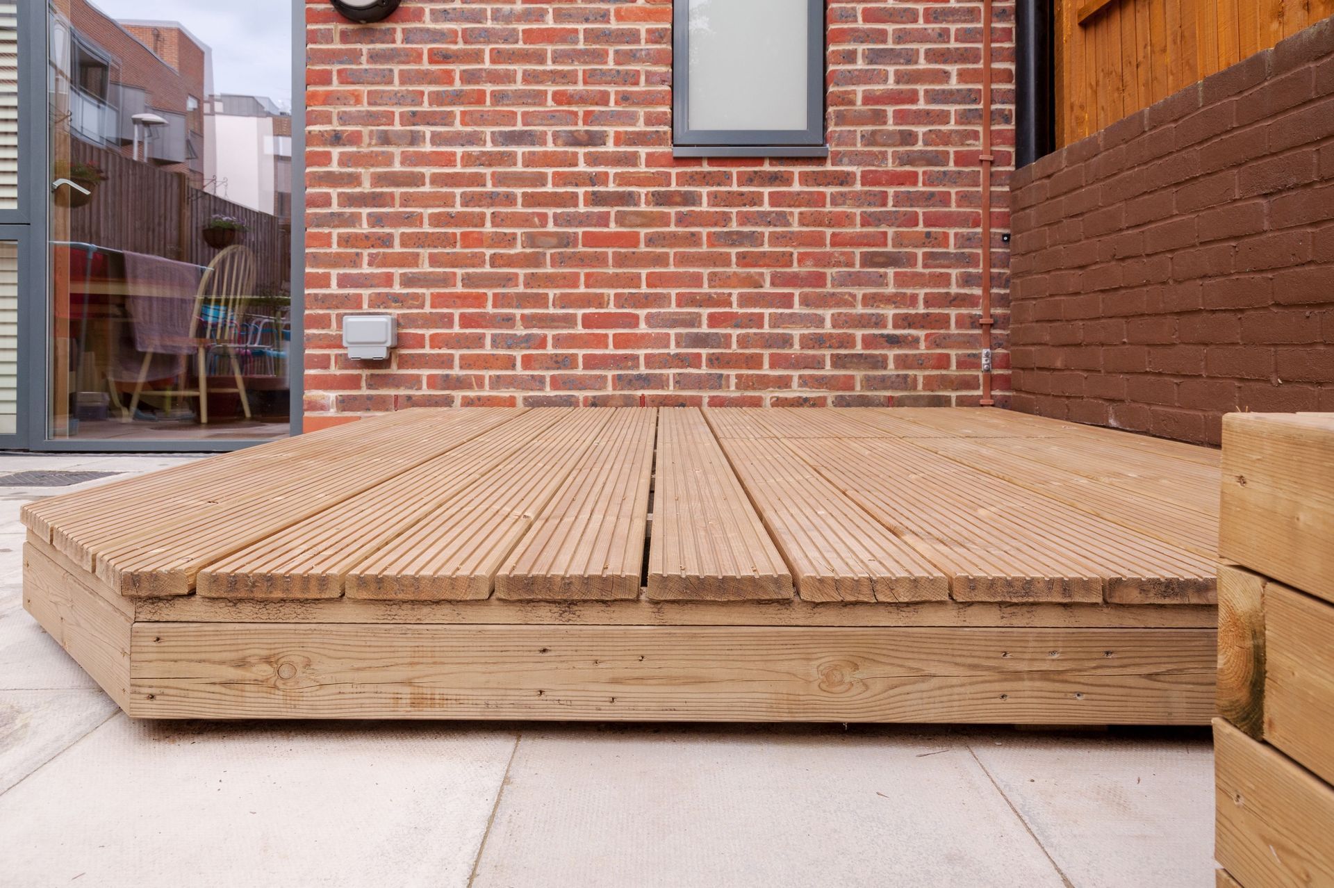 Wooden deck on a patio, with a brick wall in the background.