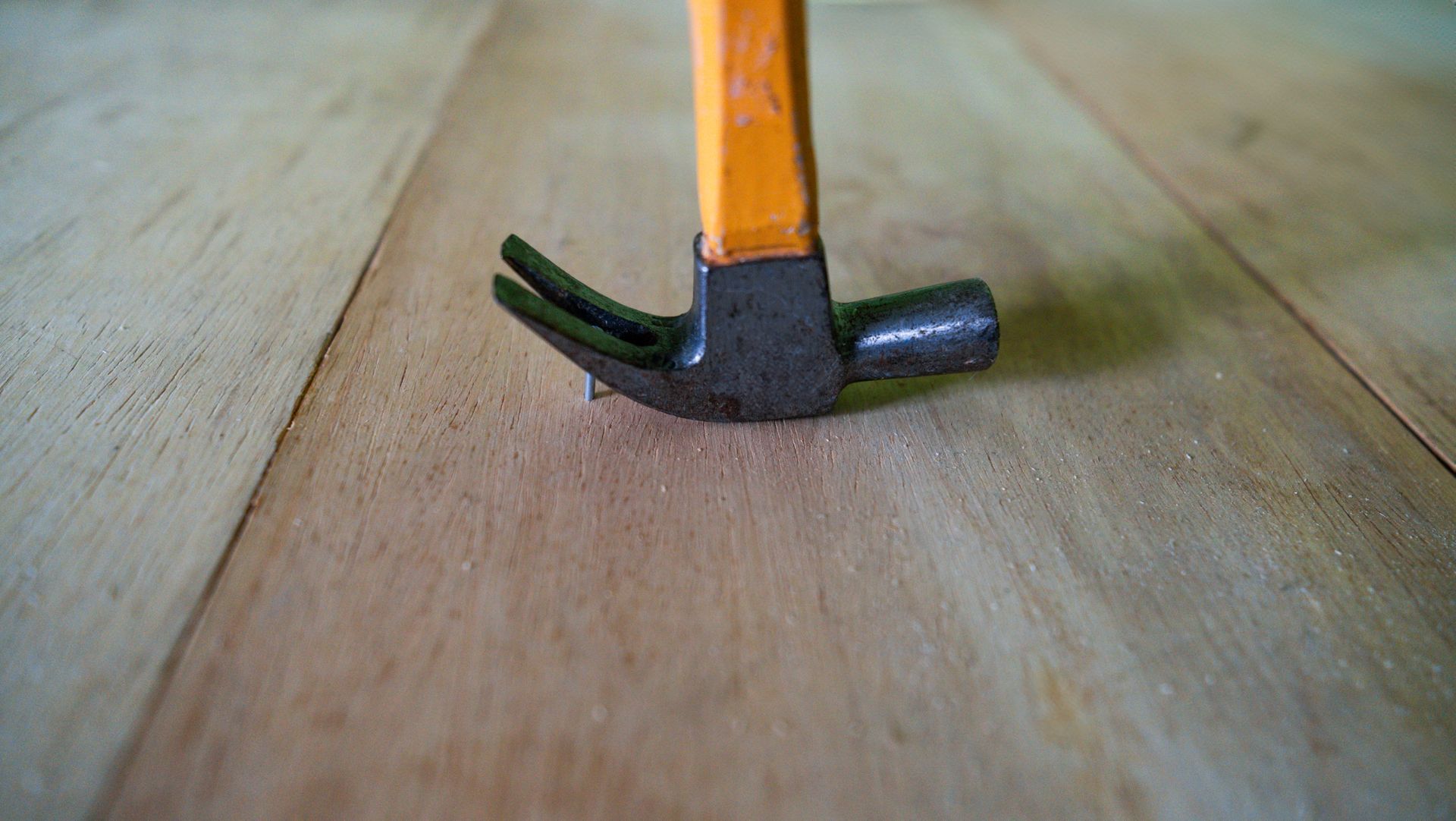 Close-up of a hammer with an orange handle on a wooden surface.