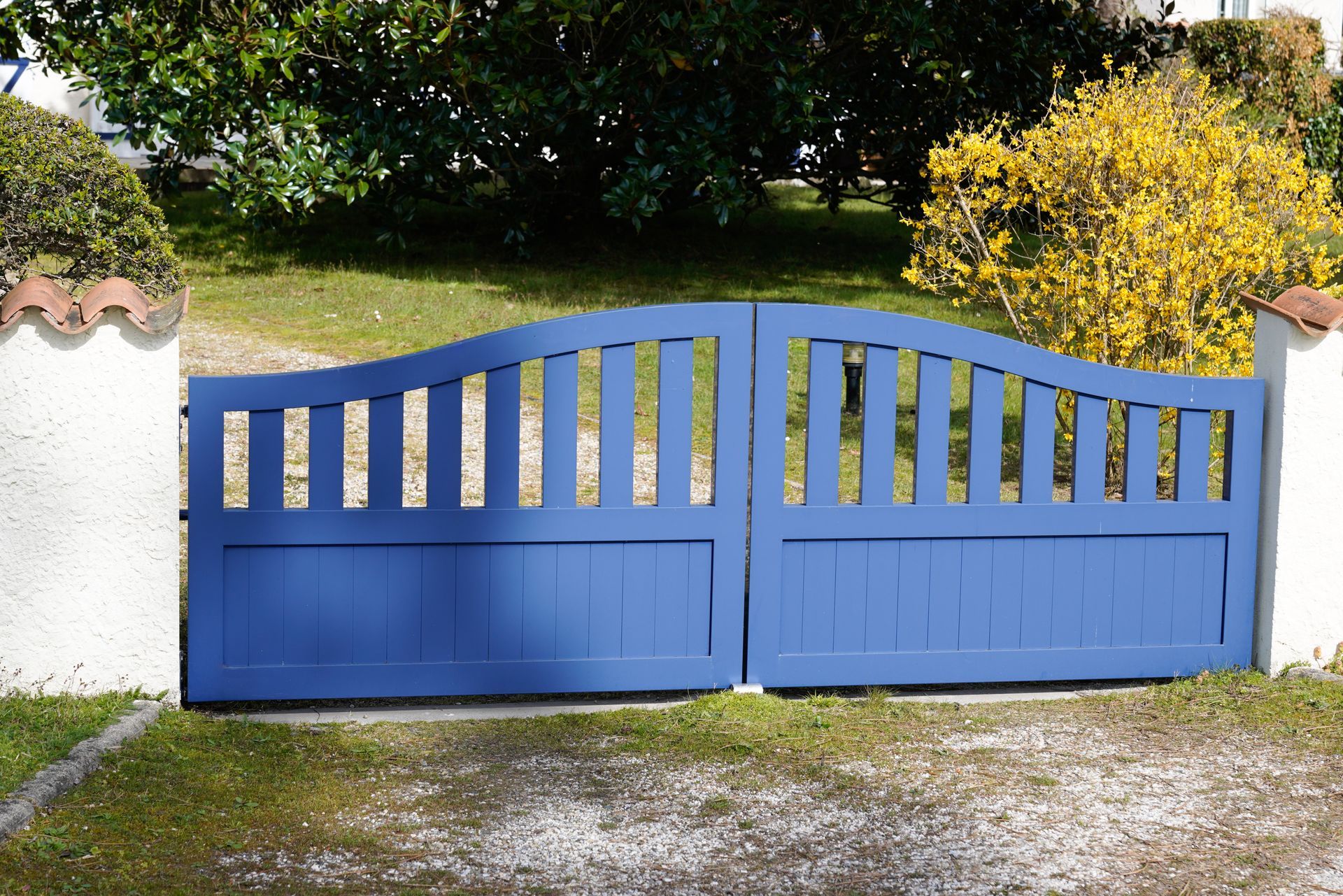 Blue wooden gate, set between white pillars with red tile tops, opening onto a grassy area.
