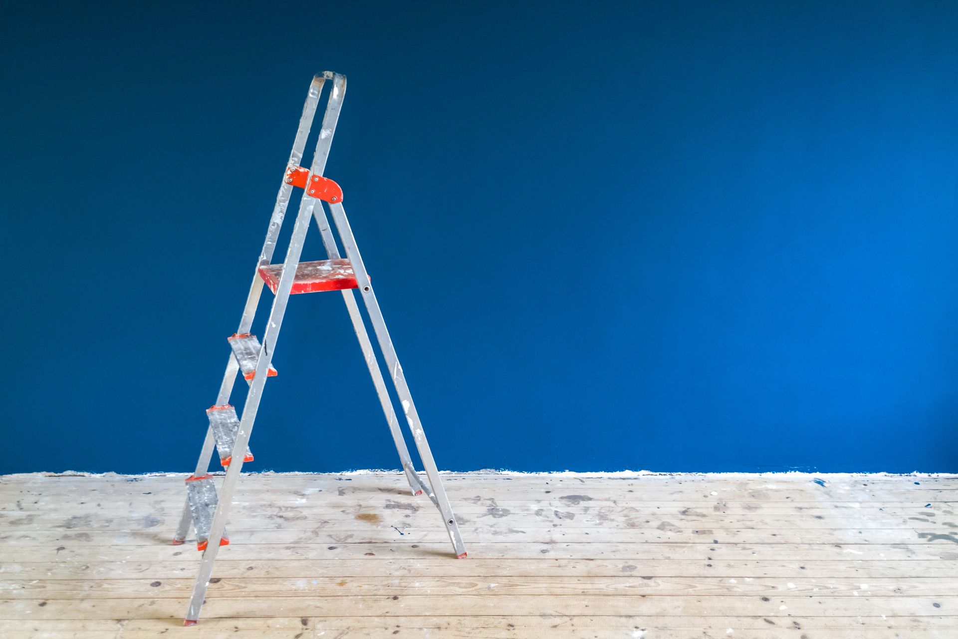 Silver ladder leaning against a blue wall on a wooden floor.