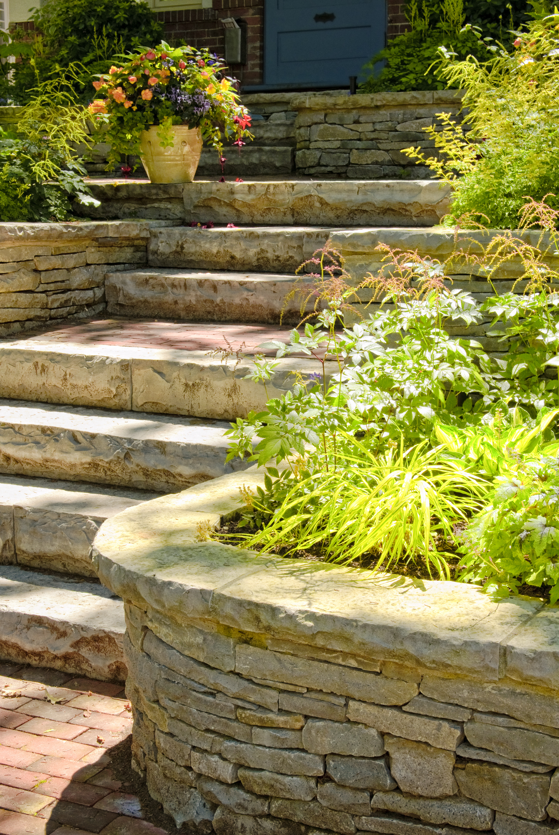 A stone wall surrounds a set of stairs leading up to a house.