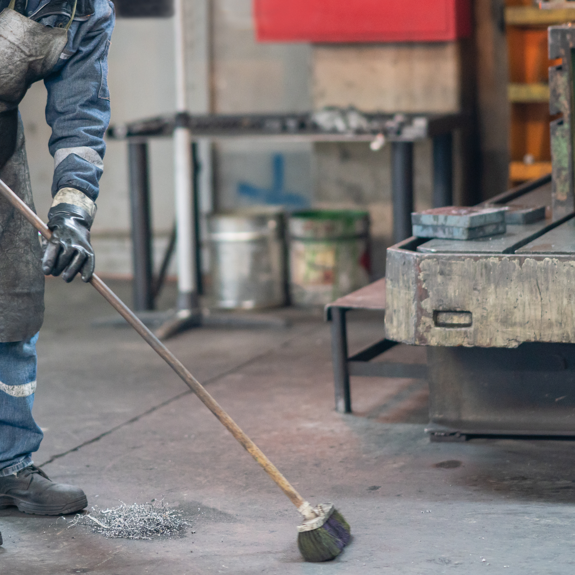 A man is sweeping the floor with a broom in a factory. Jarvis & Son Renovations,