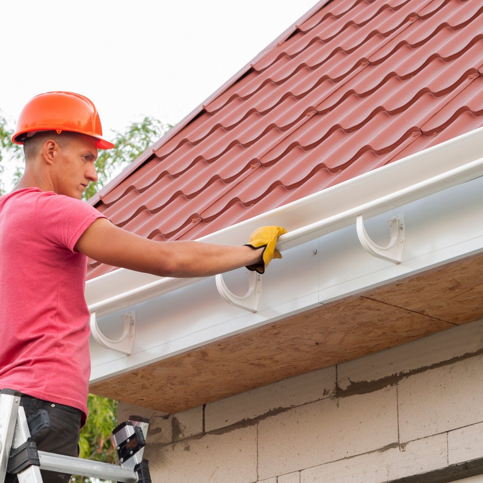 A man is standing on a ladder fixing a gutter on a roof. Jarvis & Son Renovations,