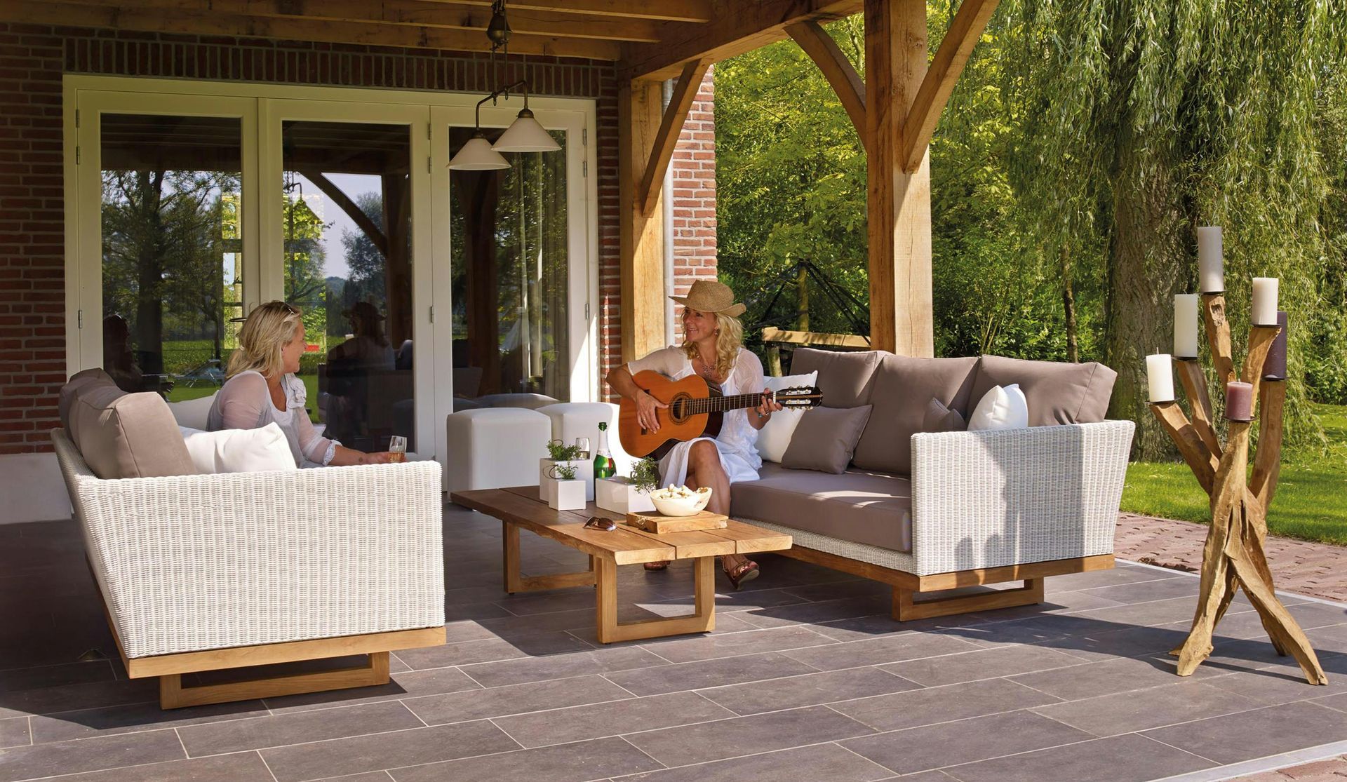 A woman is sitting on a couch on a wooden deck with a garden building