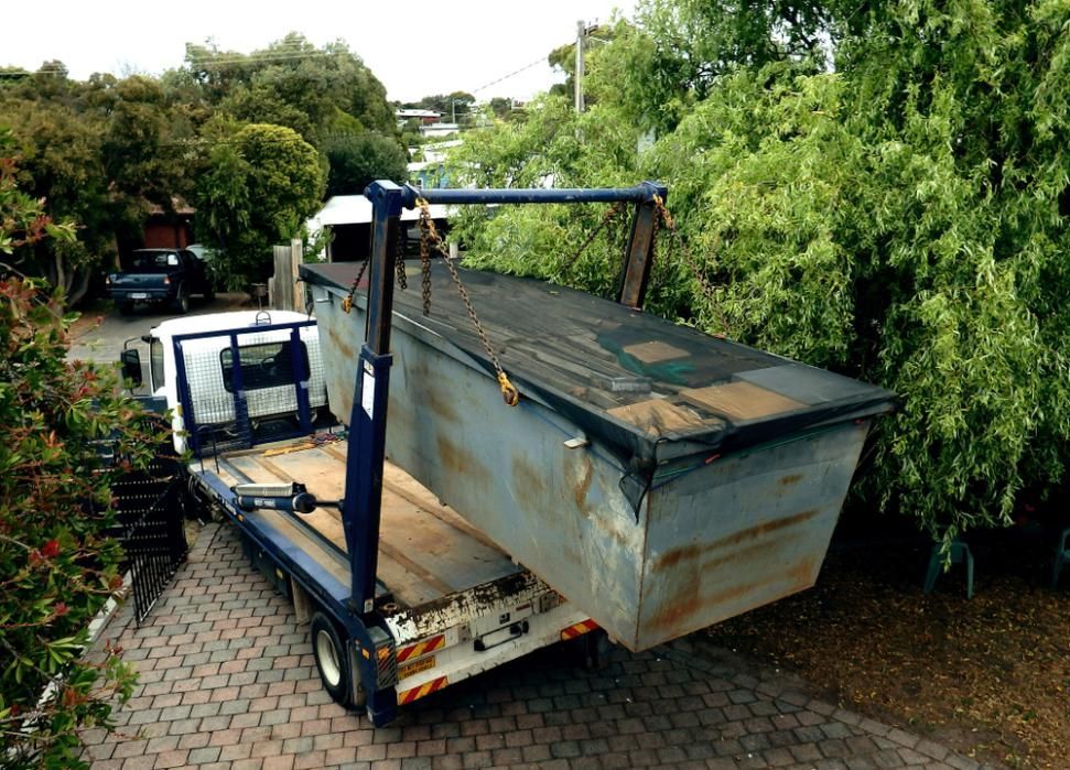 A Dumpster Is Being Loaded Onto A Truck In A Driveway — Ahern's Removals In Brisbane, QLD