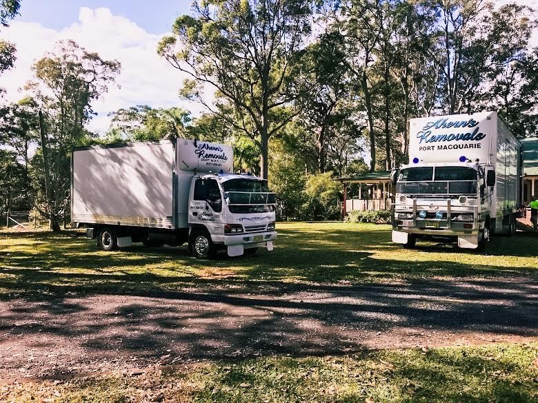 Two Moving Trucks Are Parked Next To Each Other In A Grassy Area — Ahern's Removals In Taree, NSW