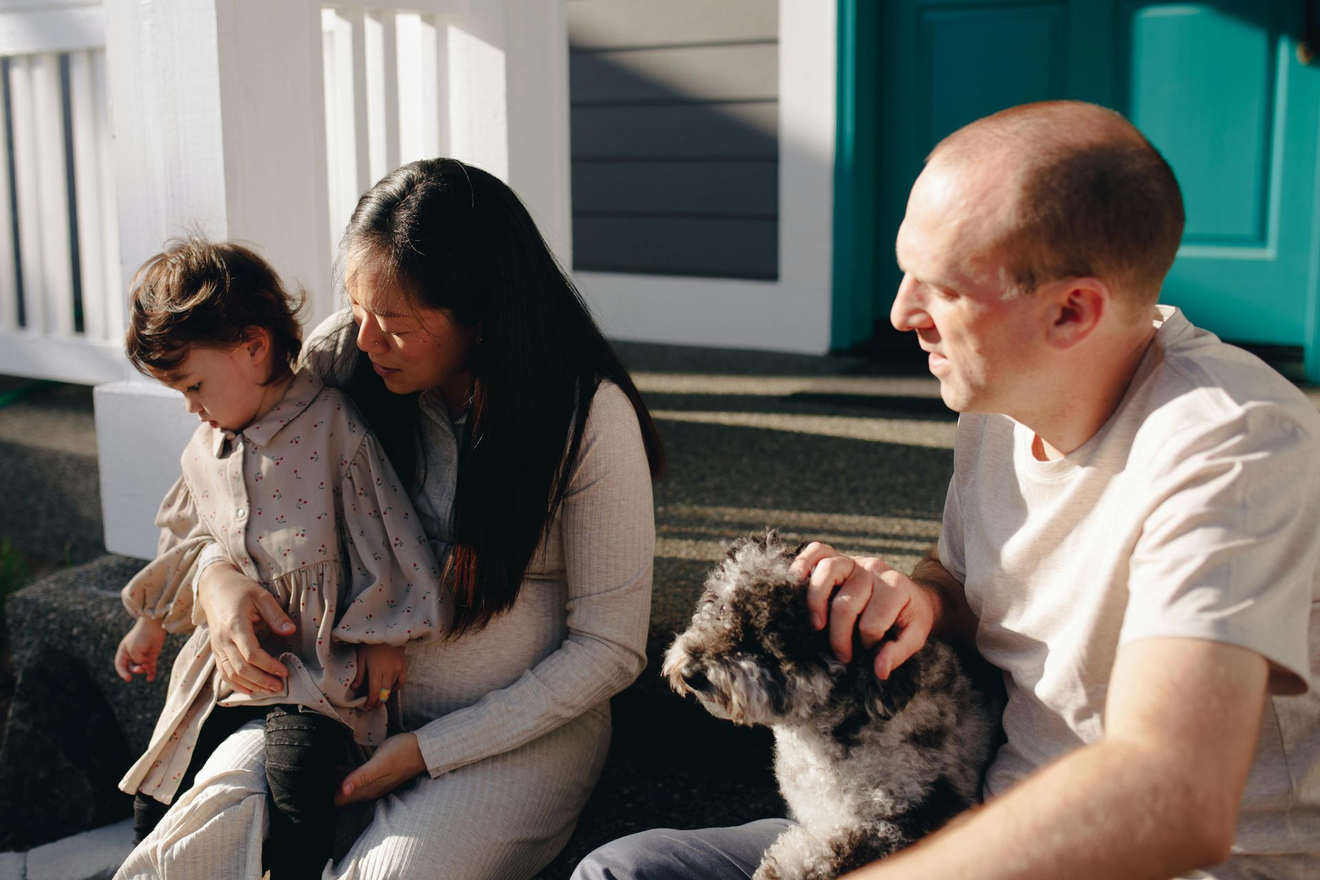 A family is sitting on the steps of their house with a dog.