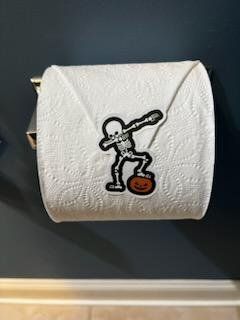 Toilet paper roll with skeleton dabbing on a pumpkin patch, attached to a wall.
