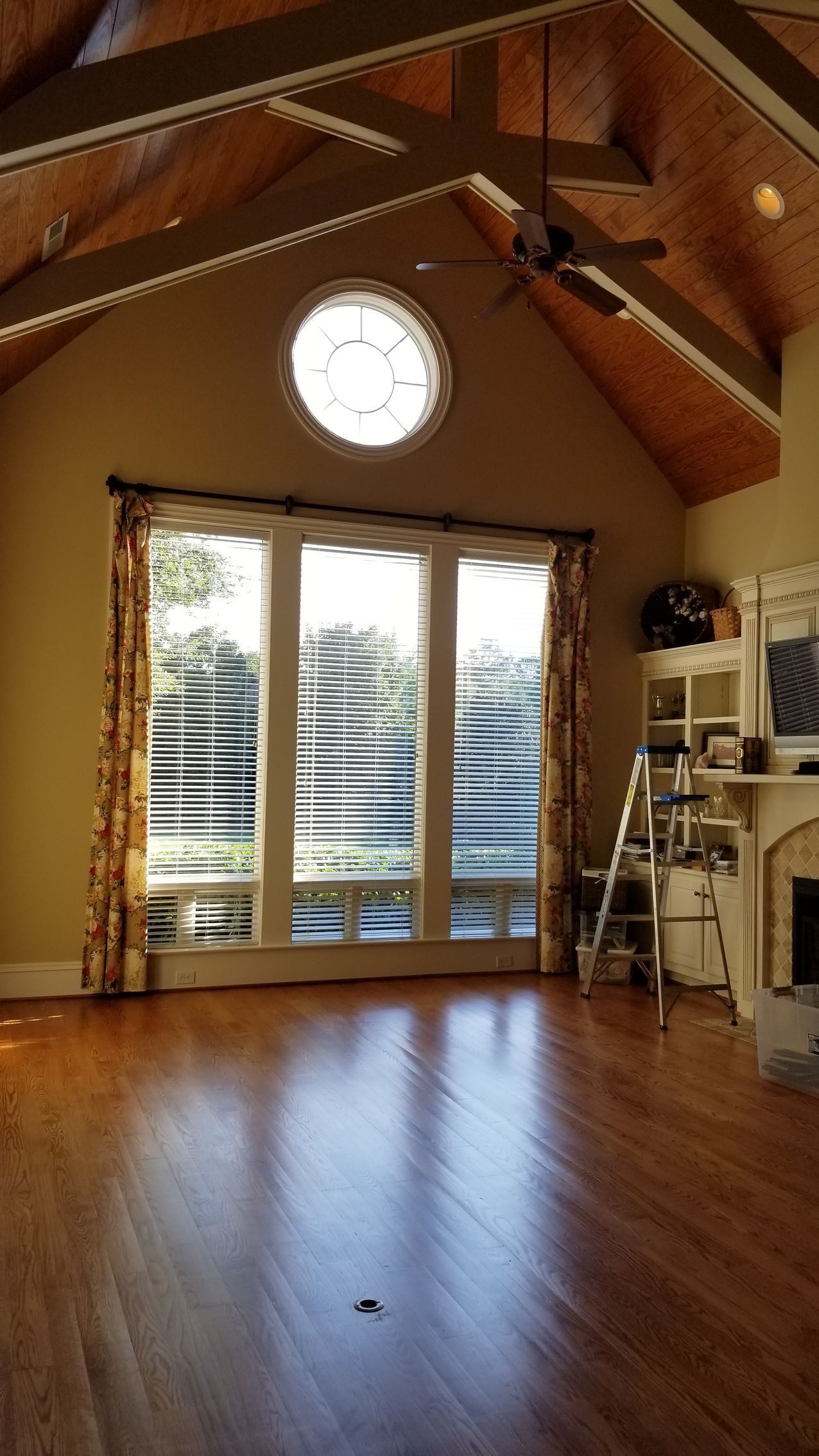 Spacious room with tall, wood-beamed ceiling, large windows, hardwood floors, and built-in shelving.