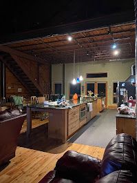 Large kitchen with island, cabinets, and a leather couch. Wooden stairs lead up to a second floor.
