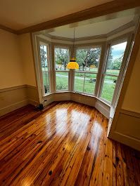 Hardwood floor in room with a bay window overlooking a green yard, yellow light fixture.