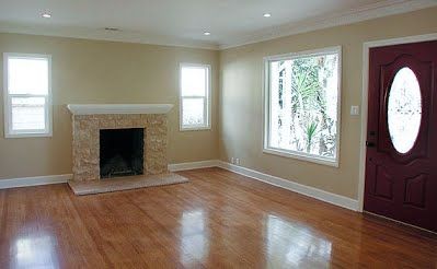 Empty living room with wood flooring, stone fireplace, and burgundy front door.