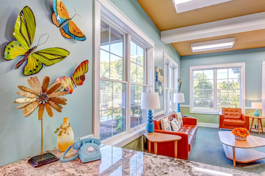 Colorful living room with butterflies, windows, red sofa, blue rug, and flower.
