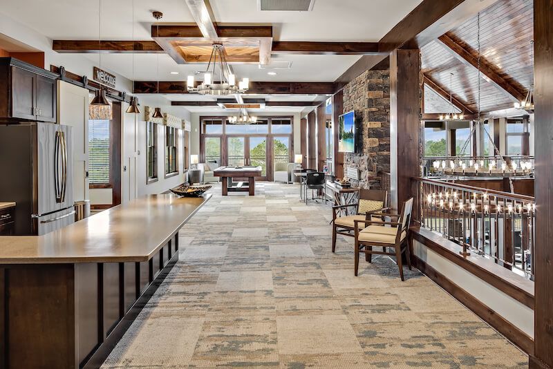 Spacious community room with a kitchen, pool table, seating, and large windows.