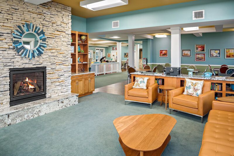 Cozy lounge with fireplace, armchairs, and a sofa. Light blue walls, green carpet, and wooden accents.