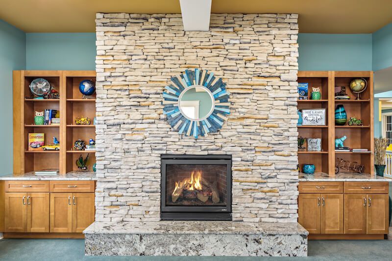 Fireplace with stone surround, built-in bookshelves, blue mirror, and granite hearth in a room with blue walls.