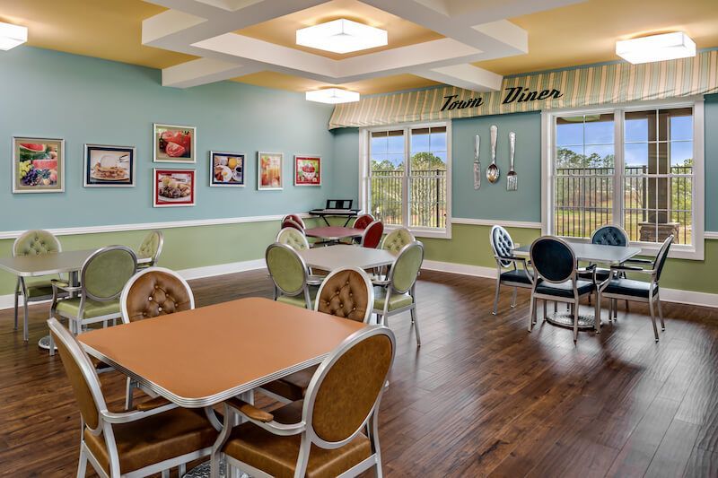Retro diner dining room with tables, chairs, and vintage decor; framed art on walls, large windows.