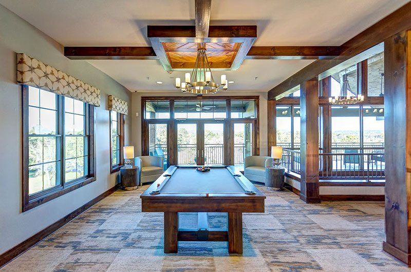 A billiards room with a pool table, two chairs, windows, and wooden accents; outdoors view.