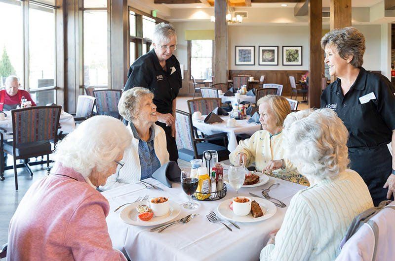Women at a table in a restaurant, served by waitresses. Light-filled dining room.