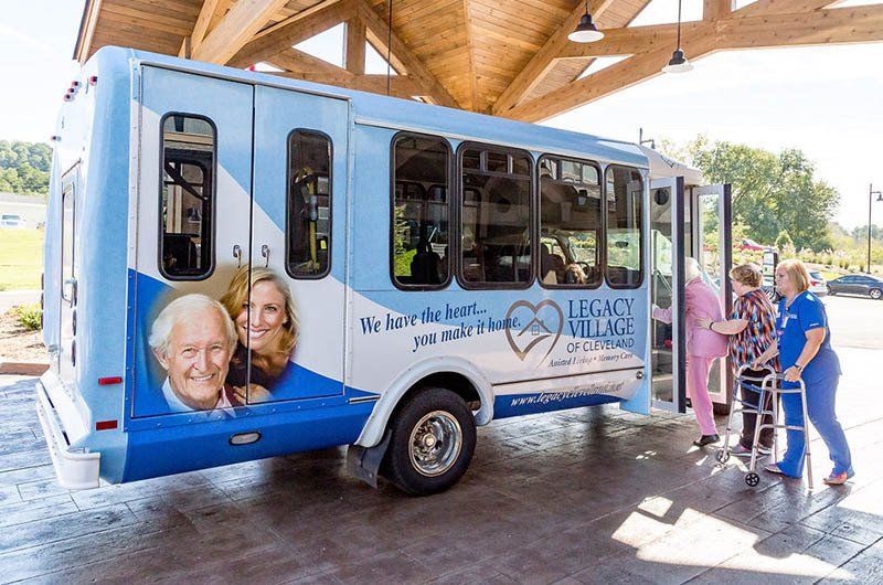 Blue shuttle bus with logo, transporting elderly people. Nurses assist with walkers.