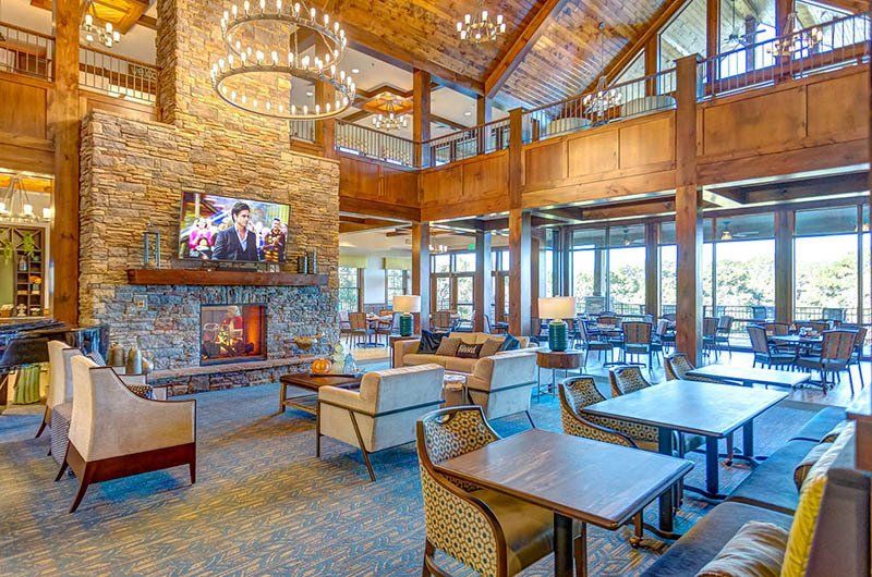 Lobby with fireplace, stone wall, wooden beams, chandeliers, seating areas, and large windows.