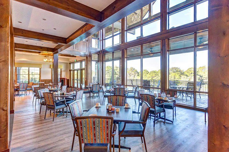 Dining room with tables, chairs, and large windows overlooking a scenic view. Wooden beams frame the space.