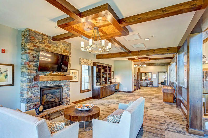 Living room with stone fireplace, sofas, wooden beams, and chandelier.