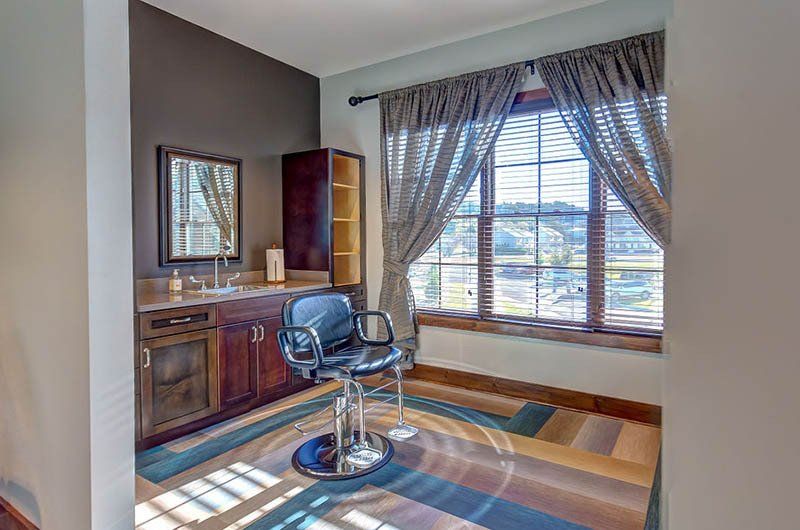 Salon station with chair, mirror, cabinets, window with blinds and patterned rug.