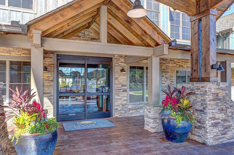 Entrance of a stone-clad building with glass doors, wooden beams, and potted plants in front.
