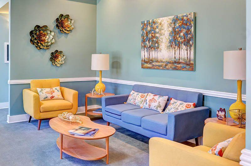 Living room with blue walls, yellow furniture, art and lamps.
