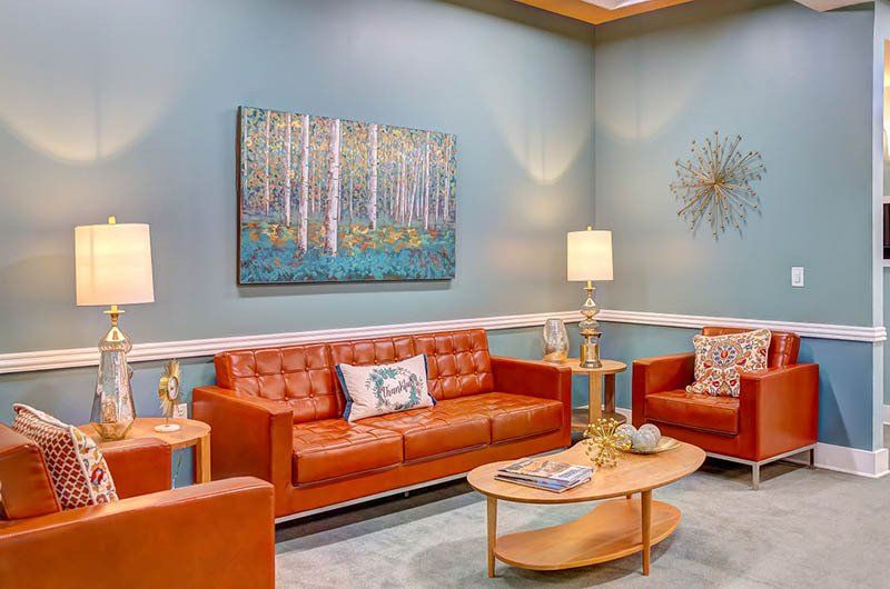 Orange leather seating in a waiting area with teal walls, artwork, lamps, and an oval coffee table.