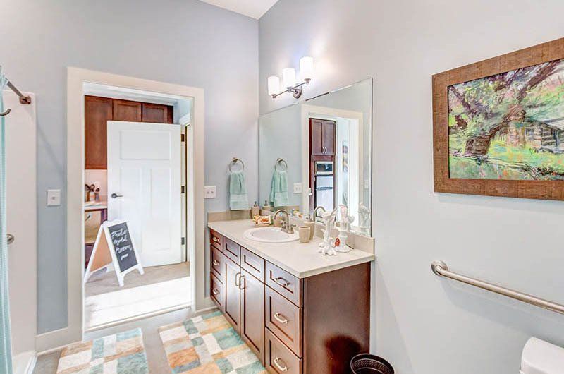 Bathroom with light blue walls, brown vanity, and open door to kitchen.