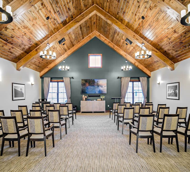 A light-filled presentation room with rows of chairs, a large screen, and a wooden ceiling.