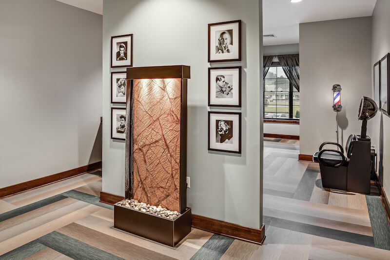 Hallway with a water fountain and framed photos; barber chair in the background.